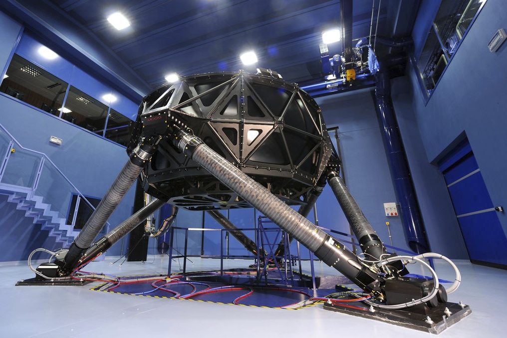 The old Ferrari F1 simulator, a massive Moog hexapod structure often called 'The Spider', used in Maranello during the 2010s to simulate G-forces. The complex hydraulic system is shown in its dedicated bay.